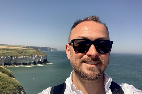 Male with sunglasses on, selfie with the cliffs behind him and blue sea